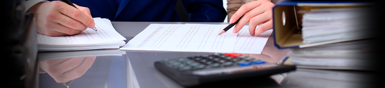 Hands writing on paperwork with calculator and gavel on desk.